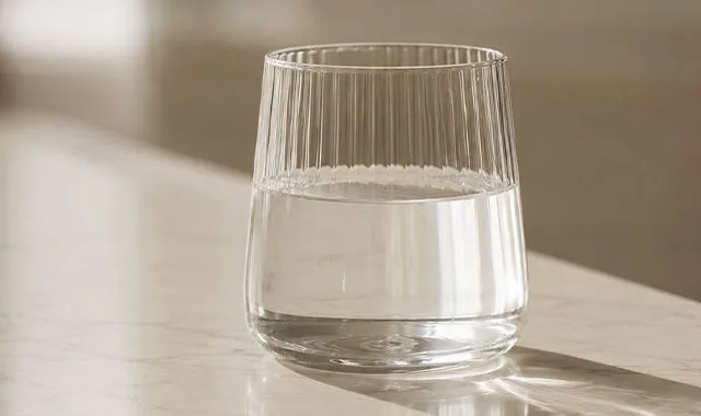 Güneş ışığı alan bir tezgahta berrak Kangen Water® dolu yivli bir bardak
